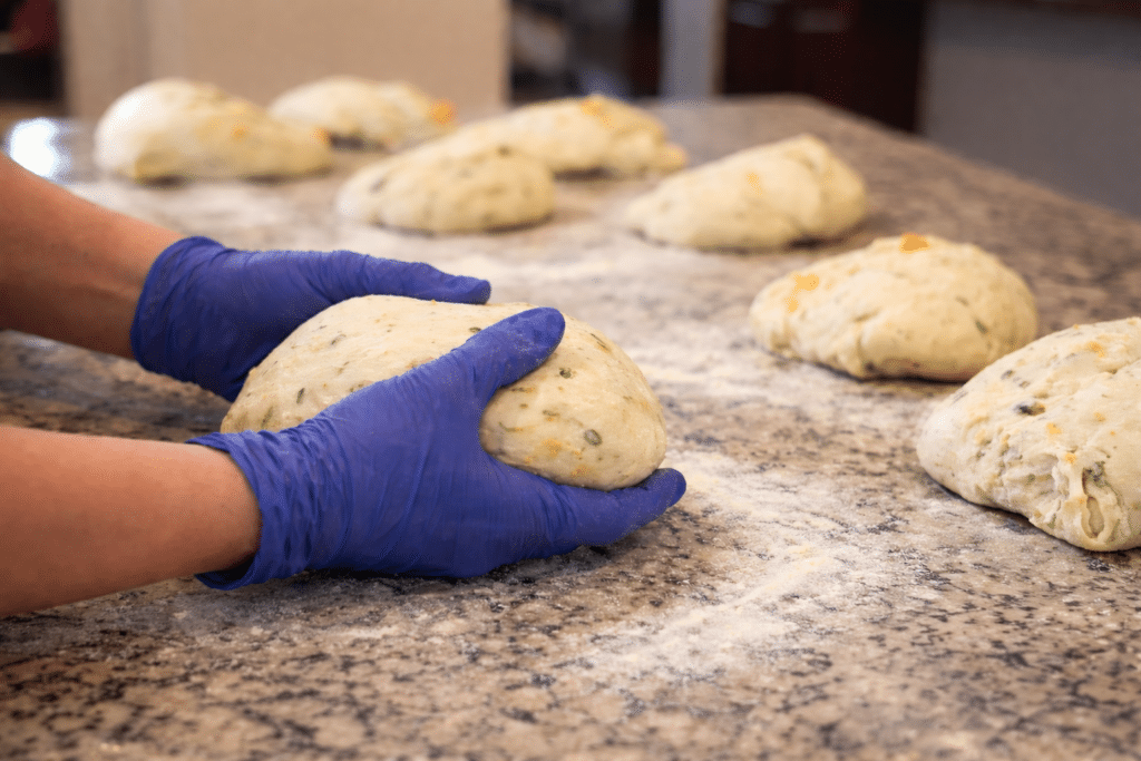 home - Hands shaping small batch sourdough dough on a floured kitchen counter